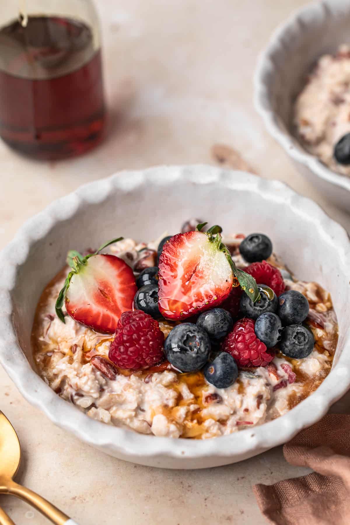A bowl of bircher muesli topped with fresh berries with a bottle of maple syrup in the background.