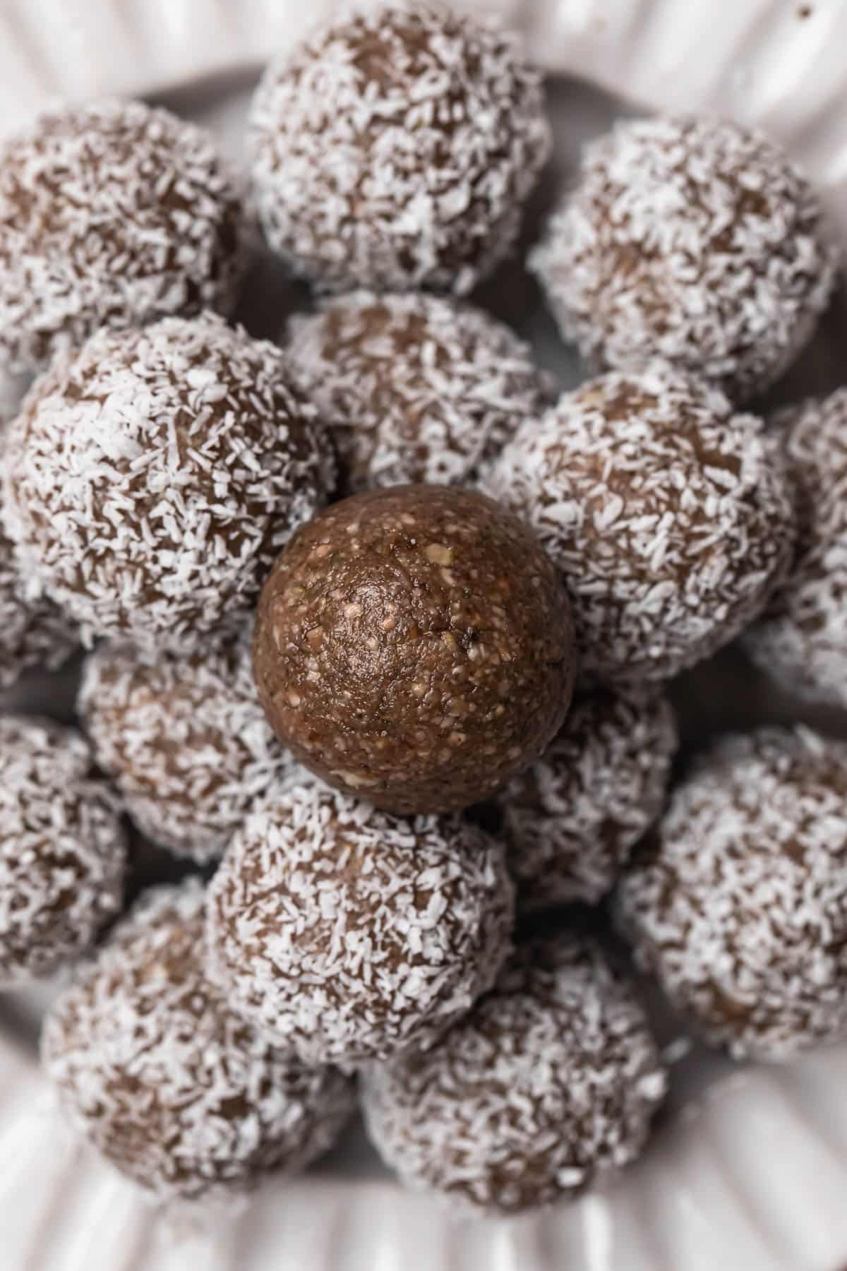 Bliss balls rolled in coconut, stacked on a white ceramic plate. The top bliss ball isn't rolled in coconut.