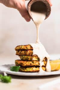 Broccoli and sweet potato fritters stacked on a plate and drizzled with lemon tahini dressing.