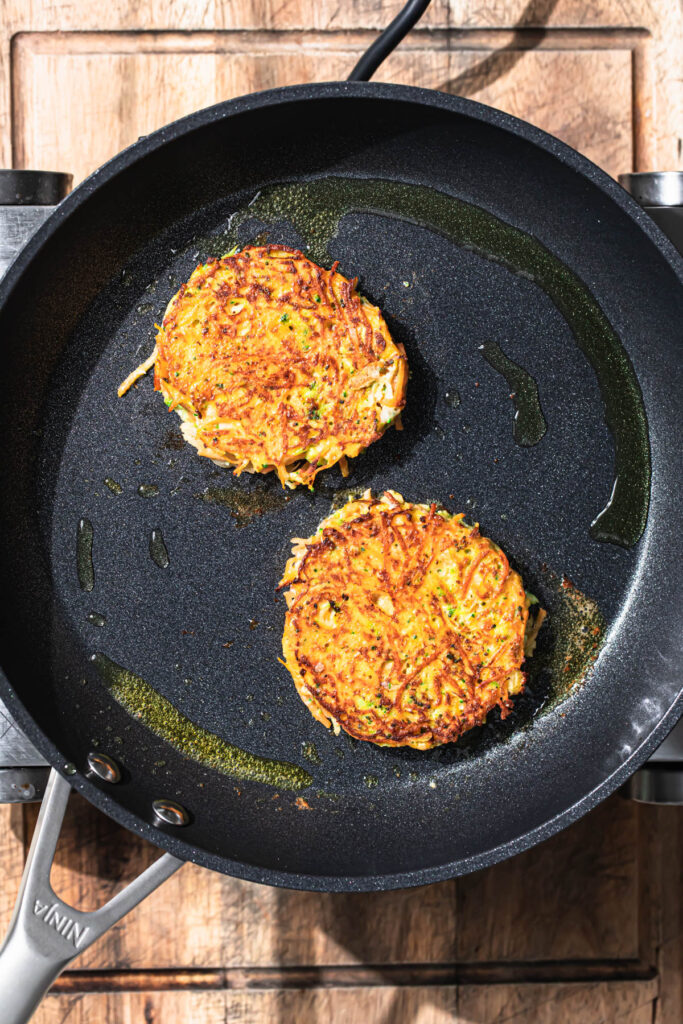 Golden brown sweet potato fritters frying in a pan.