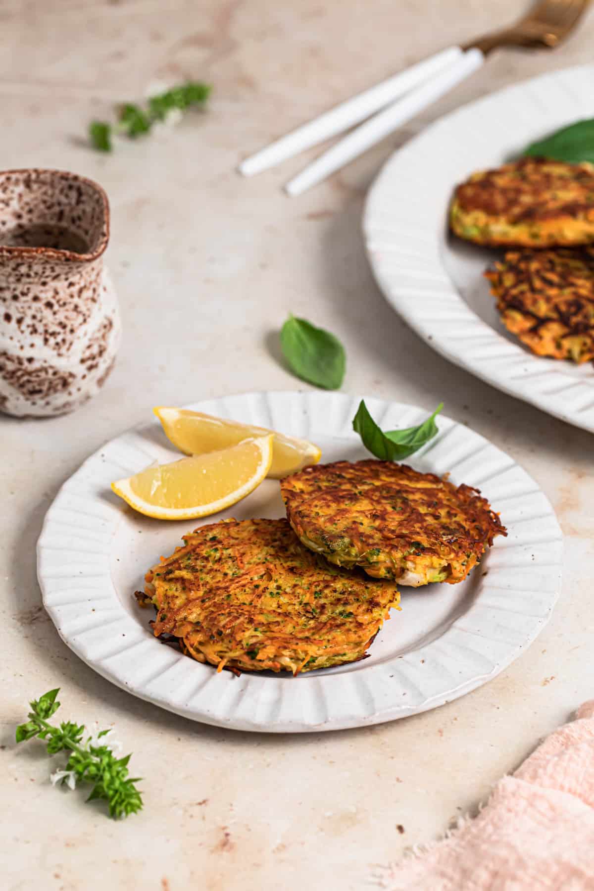 Two broccoli sweet potato fritters on a plate with lemon wedges and basil.