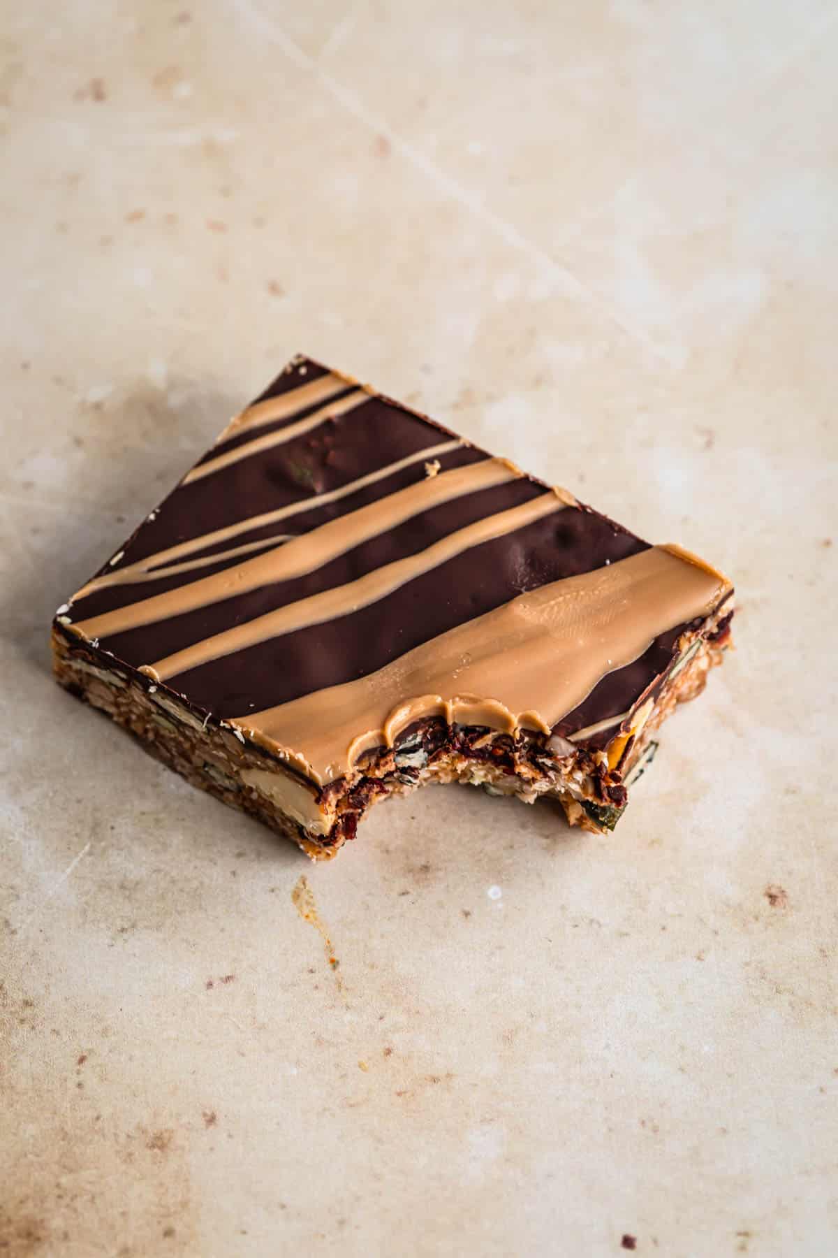 One no bake energy bar on a caramel marble backdrop, the bar has one bite taken out of it.