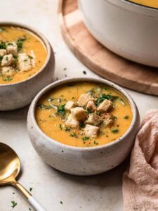 Lemony white bean soup in a handmade ceramic bowl, topped with croutons, finely chopped parsley and cracked black pepper, the white soup pot in the background.