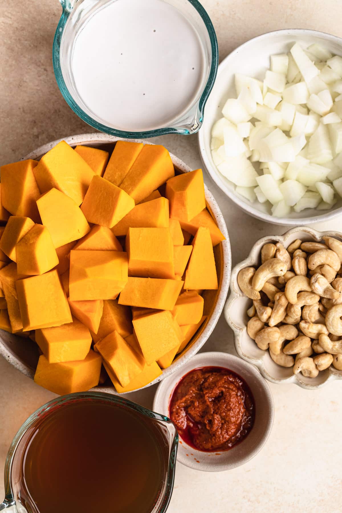 Ingredients for spicy pumpkin soup with coconut milk displayed in bowls on a peach background.