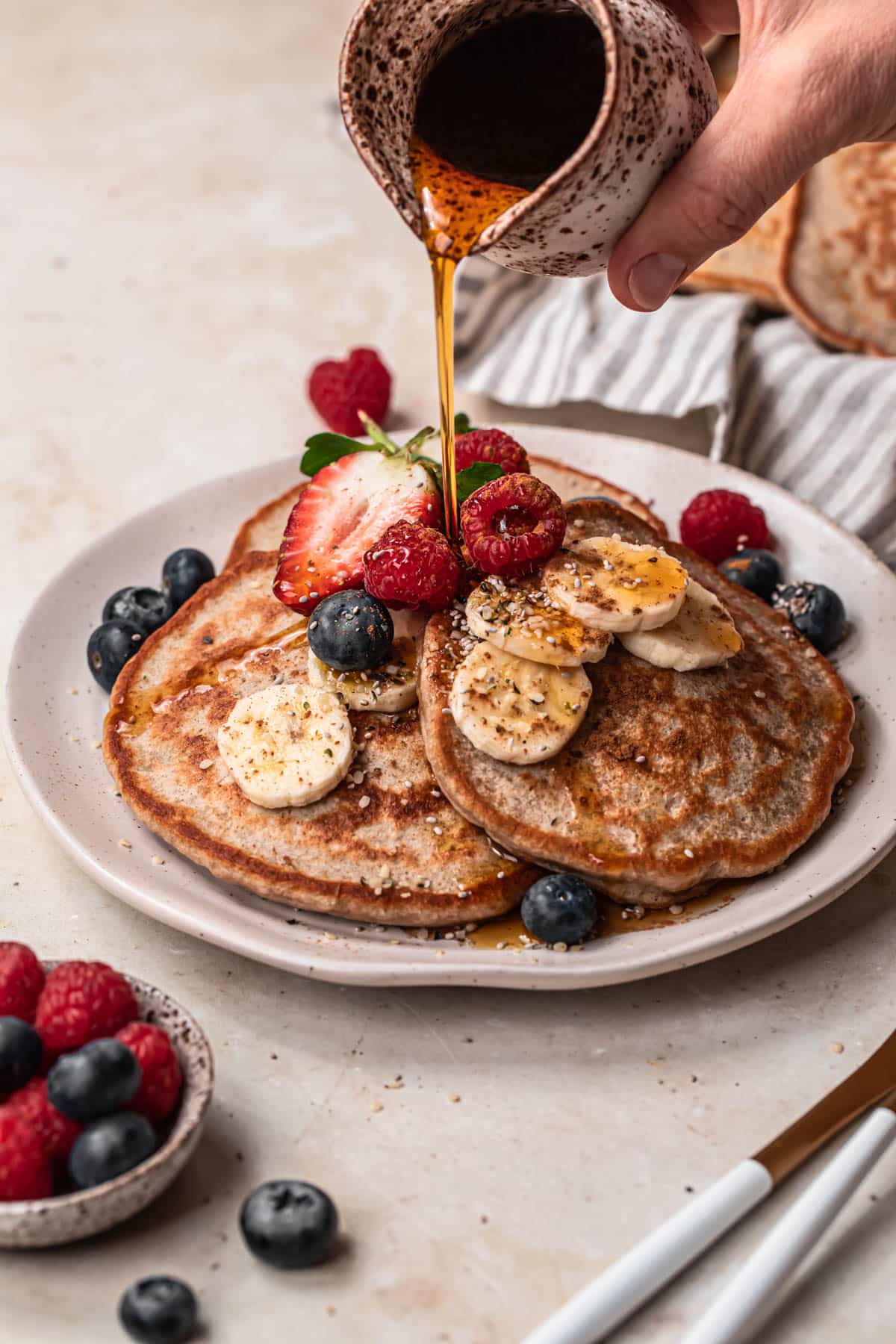 Maple syrup being poured onto a plate of banana buckwheat pancakes.