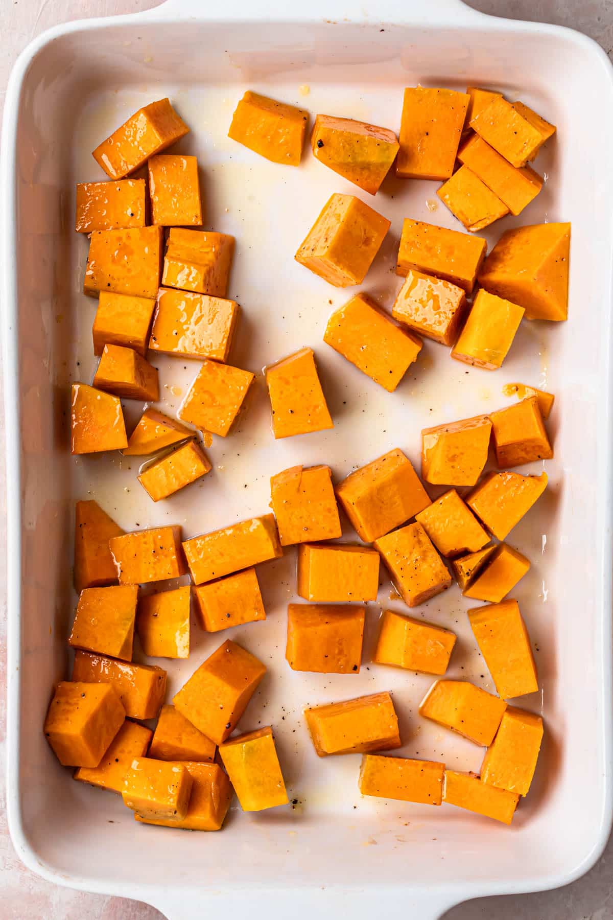 Diced pumpkin seasoned and coated in olive oil, spread out across the base of a white baking dish.