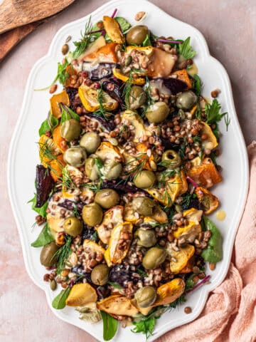 Roasted vegetable salad with olives and lentils on a white platter.