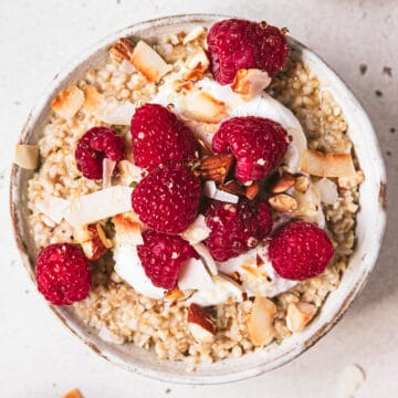 bowl of steel cut oats topped with raspberries, toasted coconut and yoghurt