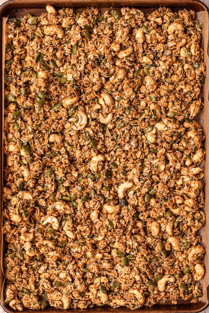 Unbaked cashew granola mixture spread out on a parchment paper lined baking tray.