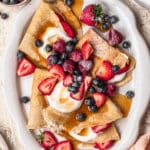 Almond flour crepes topped with fresh berries, coconut yoghurt and maple syrup on a large platter.