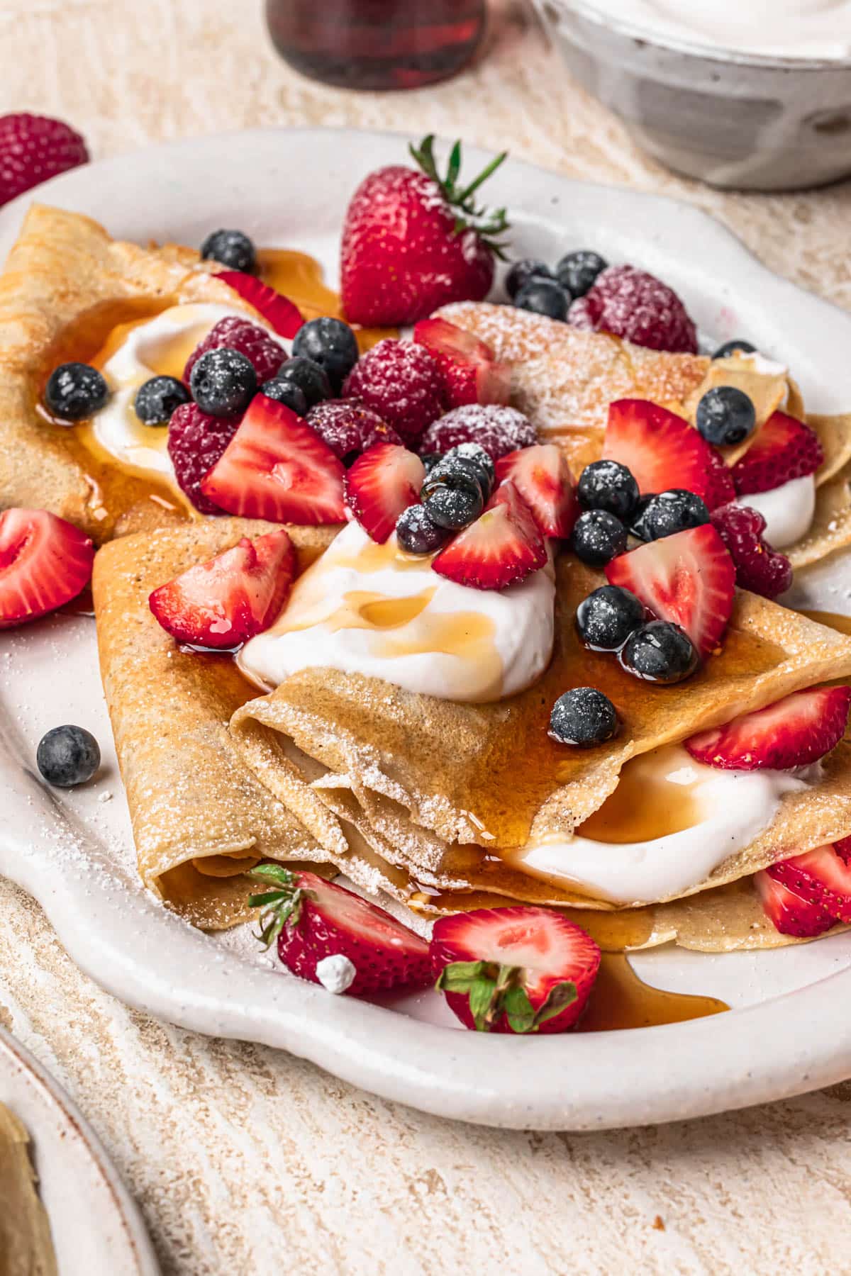 Almond flour crepes topped with fresh berries, coconut yoghurt and maple syrup on a large platter.