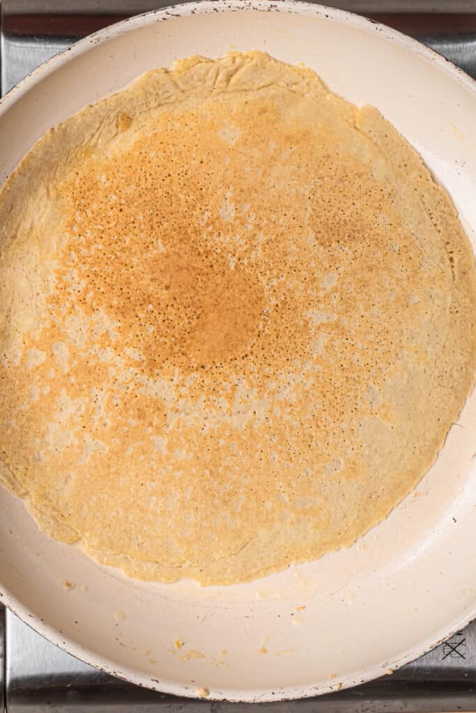 Golden brown almond flour crepe in frying pan, flipped over.