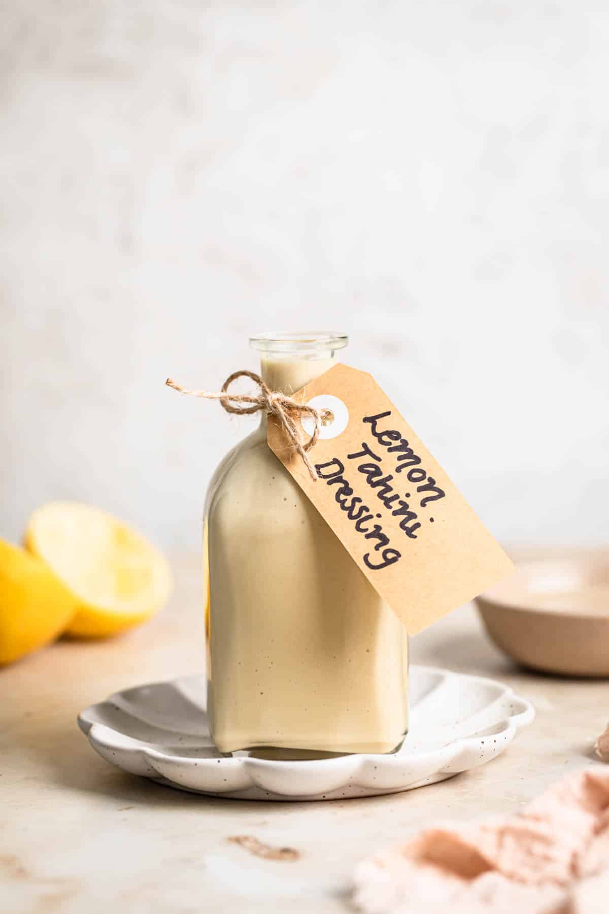Lemon tahini dressing in a glass bottle with lemons in the background.