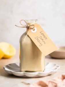Lemon tahini dressing in a glass bottle with lemons in the background.