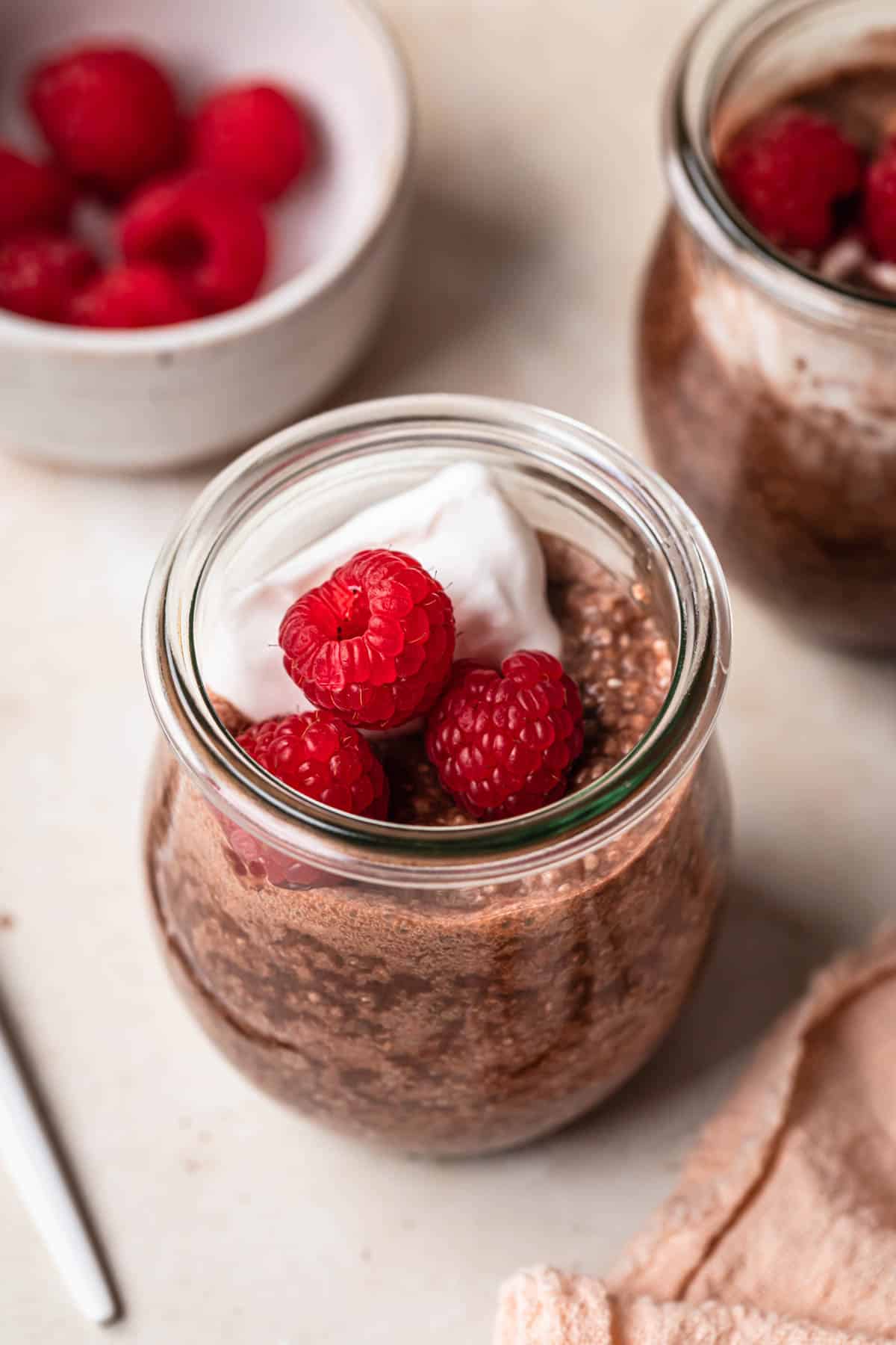 Two small jars filled with chocolate chia pudding, topped with coconut yogurt and fresh raspberries.