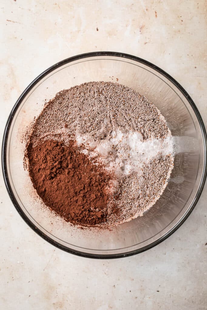 Ingredients for chocolate chia pudding with coconut milk added to a medium sized glass mixing bowl.