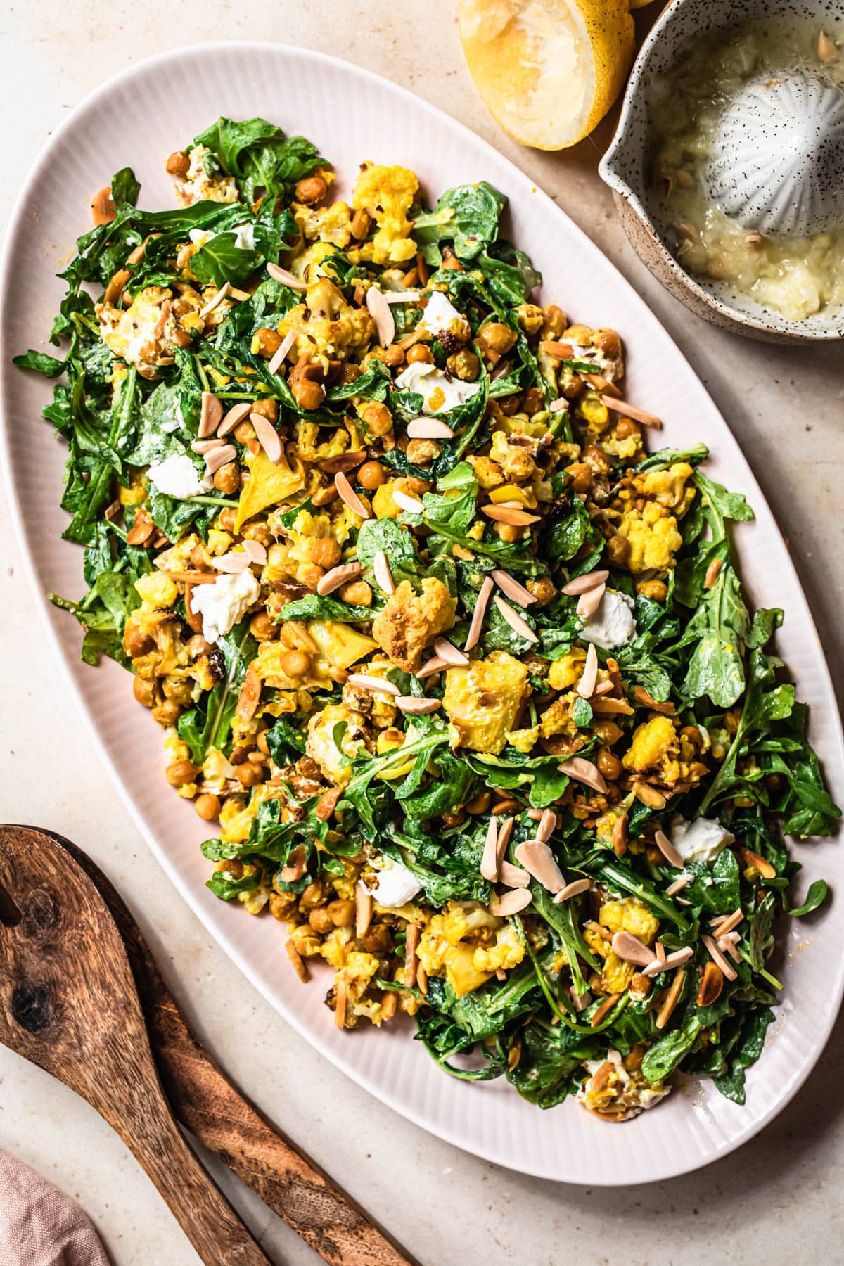 Roasted cauliflower chickpea salad with rocket and goats cheese on a pink serving platter.