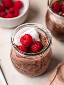 Two small jars filled with chocolate chia pudding, topped with coconut yogurt and fresh raspberries.