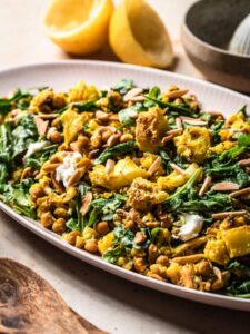 Roasted cauliflower chickpea salad with rocket and goats cheese on a pink serving platter.