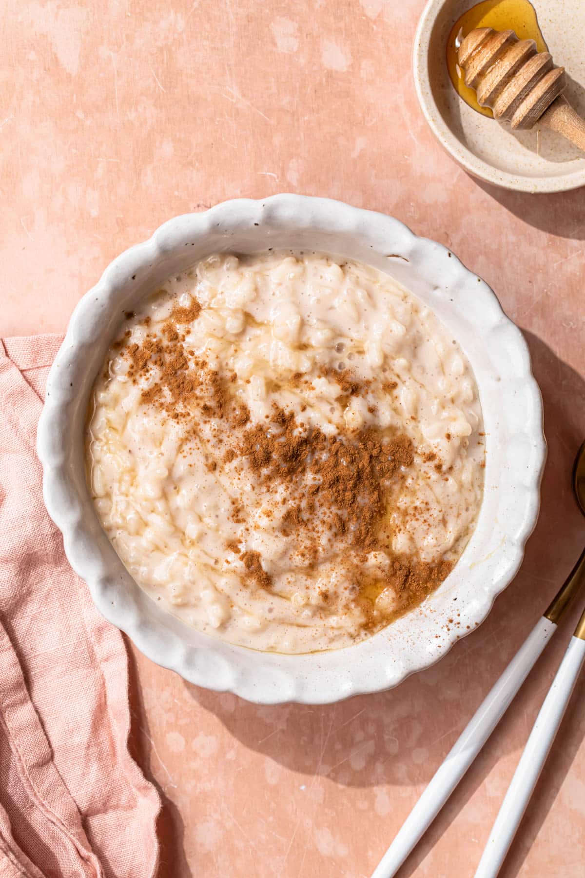 Dairy free rice pudding in a white bowl topped with cinnamon powder and honey.