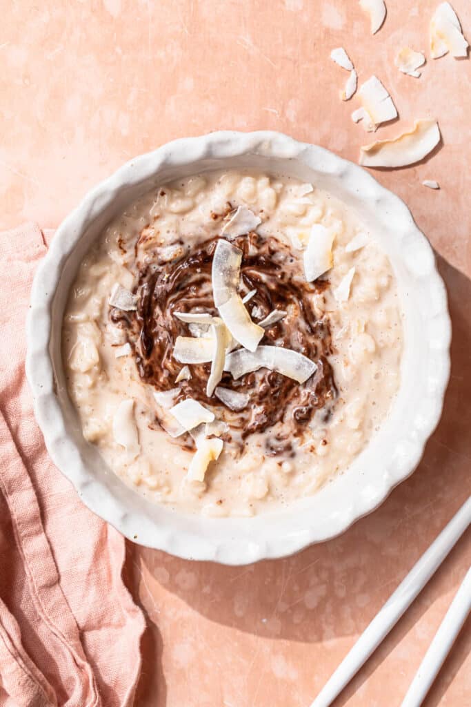 Dairy free rice pudding topped with a swirl of dark chocolate ganache and toasted coconut flakes.