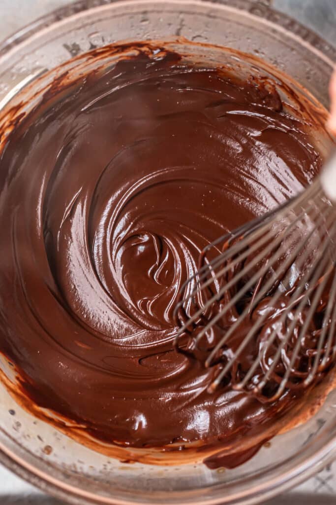Smooth and glossy dark chocolate ganache being whisked in a glass bowl.
