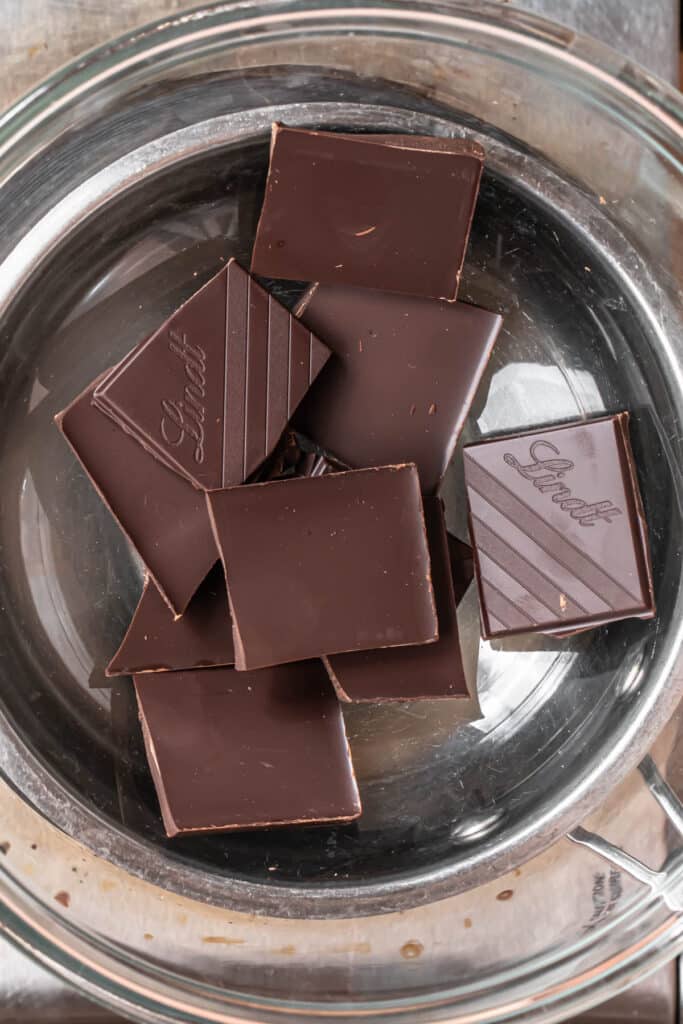 Dark chocolate added to a glass bowl atop a saucepan of water.