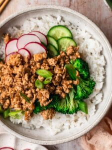 Ground chicken rice bowl with thinly sliced cucumber, radish and green onion.