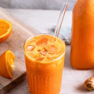 Carrot, orange, pineapple immune boosting juice in a glass with a glass straw, fresh oranges and a bottle of juice in the background.