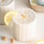 Lemon smoothie in a glass tumbler with a wedge of lemon on the glass rim.
