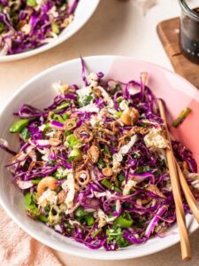 Asian coleslaw recipe served in two pink and white bowl, with chopsticks resting on the bowl at the front of the image.