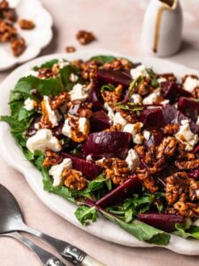 Beetroot salad with goat's cheese, honey candied walnuts and balsamic dressing, on a white serving platter.