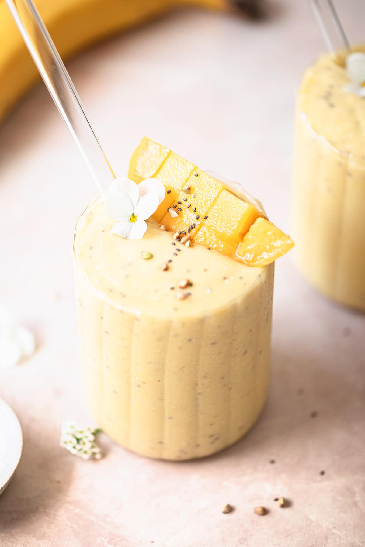 dairy free mango banana smoothie in glass with glass straw