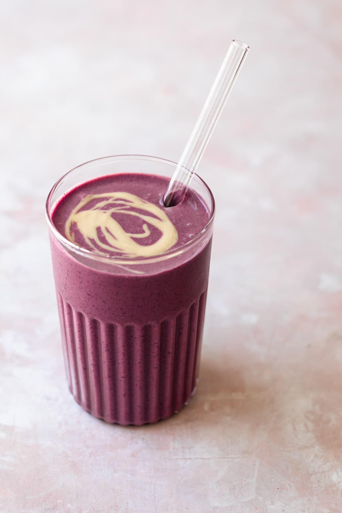 berry smoothie in glass with a swirl of tahini on top.