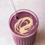 berry smoothie in glass with a swirl of tahini on top.