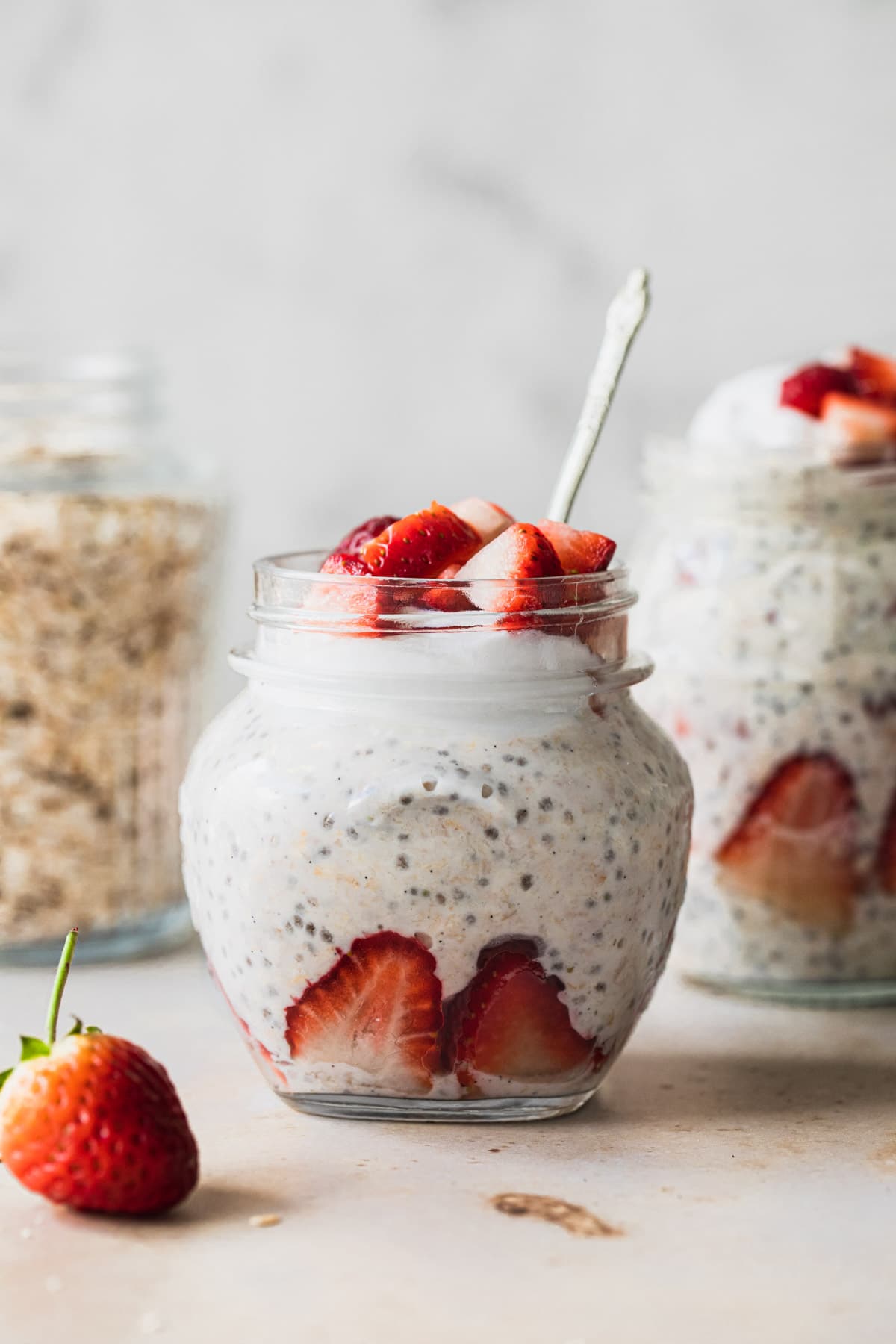 strawberry overnight oats in a small jar, with rolled oats in a jar in the background