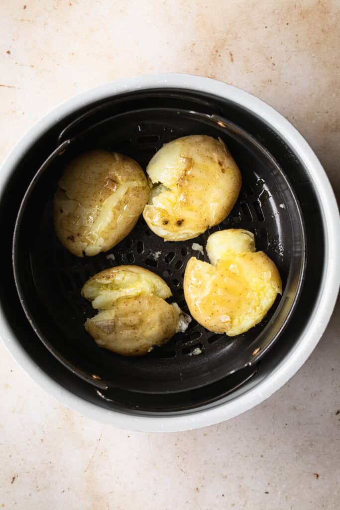 boiled potatoes in air fryer basket that have been squashed
