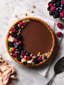 Vegan chocolate tart topped with berries and hazelnuts.