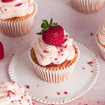 gluten free strawberry cupcakes on a white and pink backdrop with a strawberry placed on top of the strawberry cream cheese frosting.