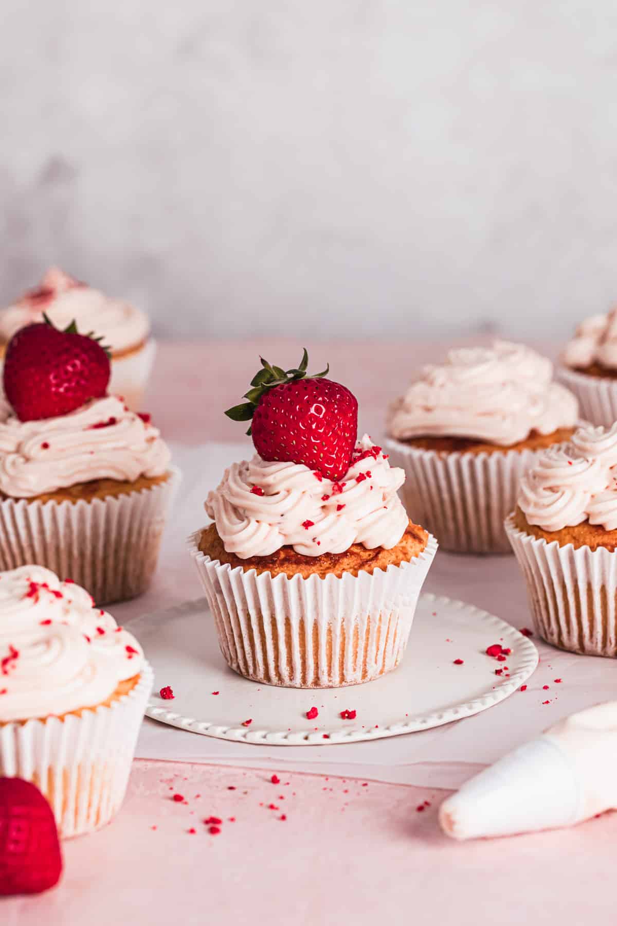 gluten free strawberry cupcakes on a white and pink backdrop with a strawberry placed on top of the frosting.