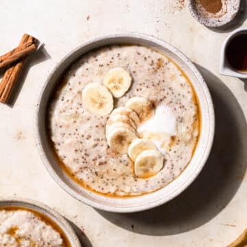 Two bowls of banana porridge, topped with banana slices, coconut yoghurt, cinnamon powder and pure maple syrup.