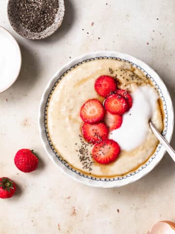 A bowl filled with egg porridge, topped with coconut yoghurt, chia seeds and strawberries.
