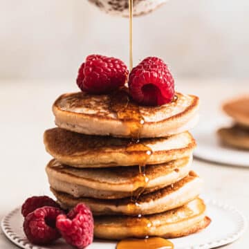 Low fodmap pancakes stacked on a white plate, maple syrup being poured over the top.