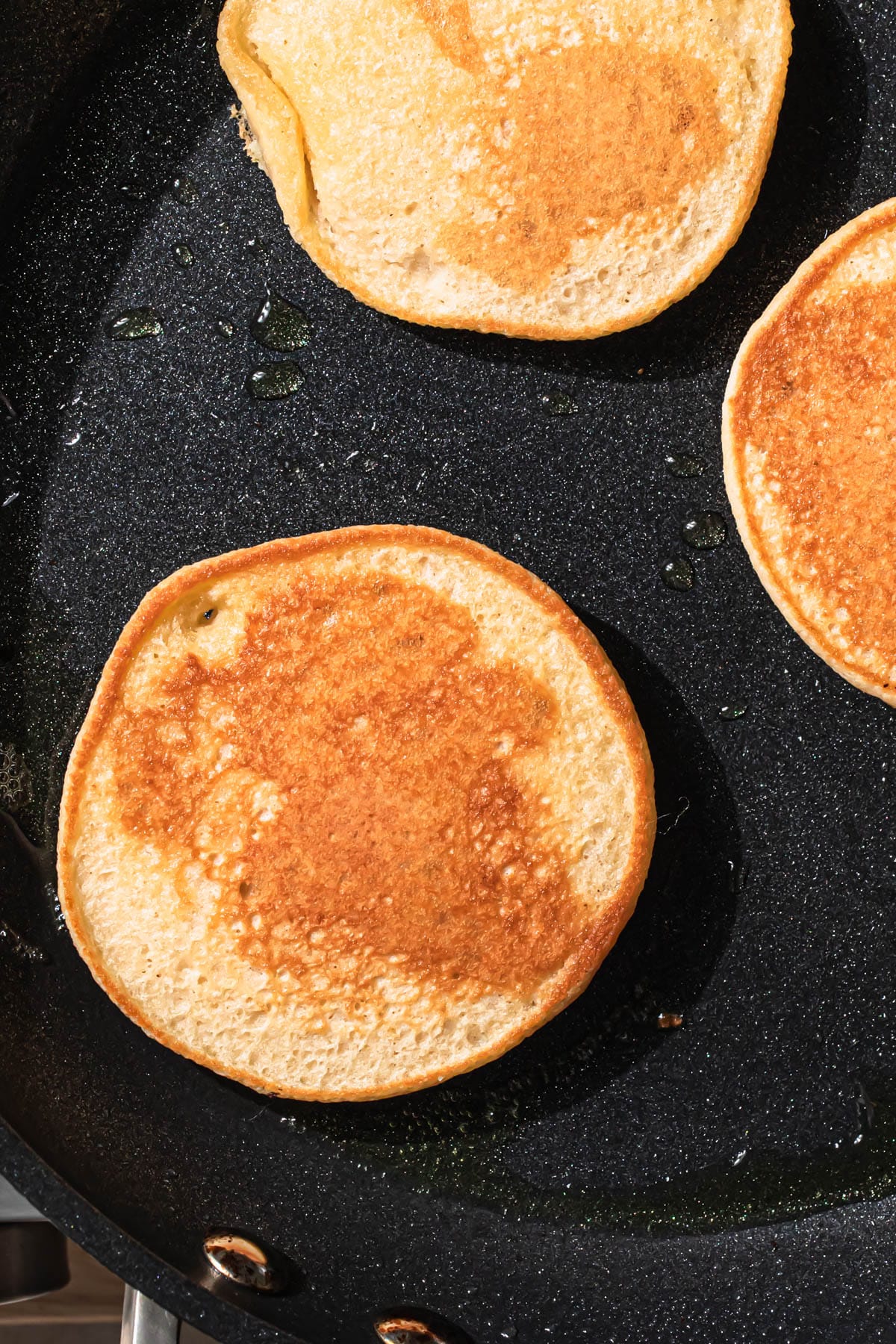 Golden brown pancakes frying in a frypan.
