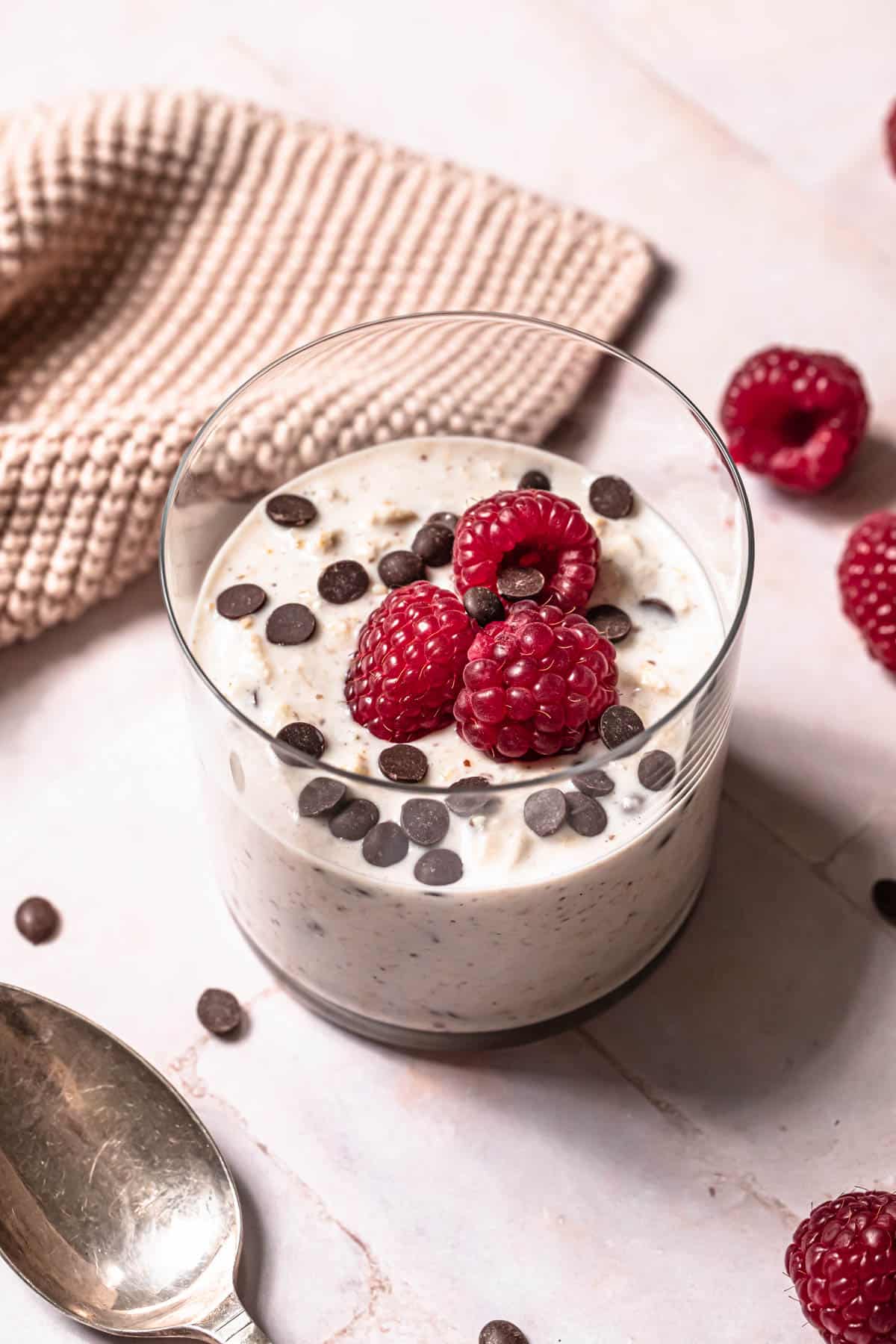 Chocolate chip overnight oats in a glass topped with chocolate chips and fresh raspberries.