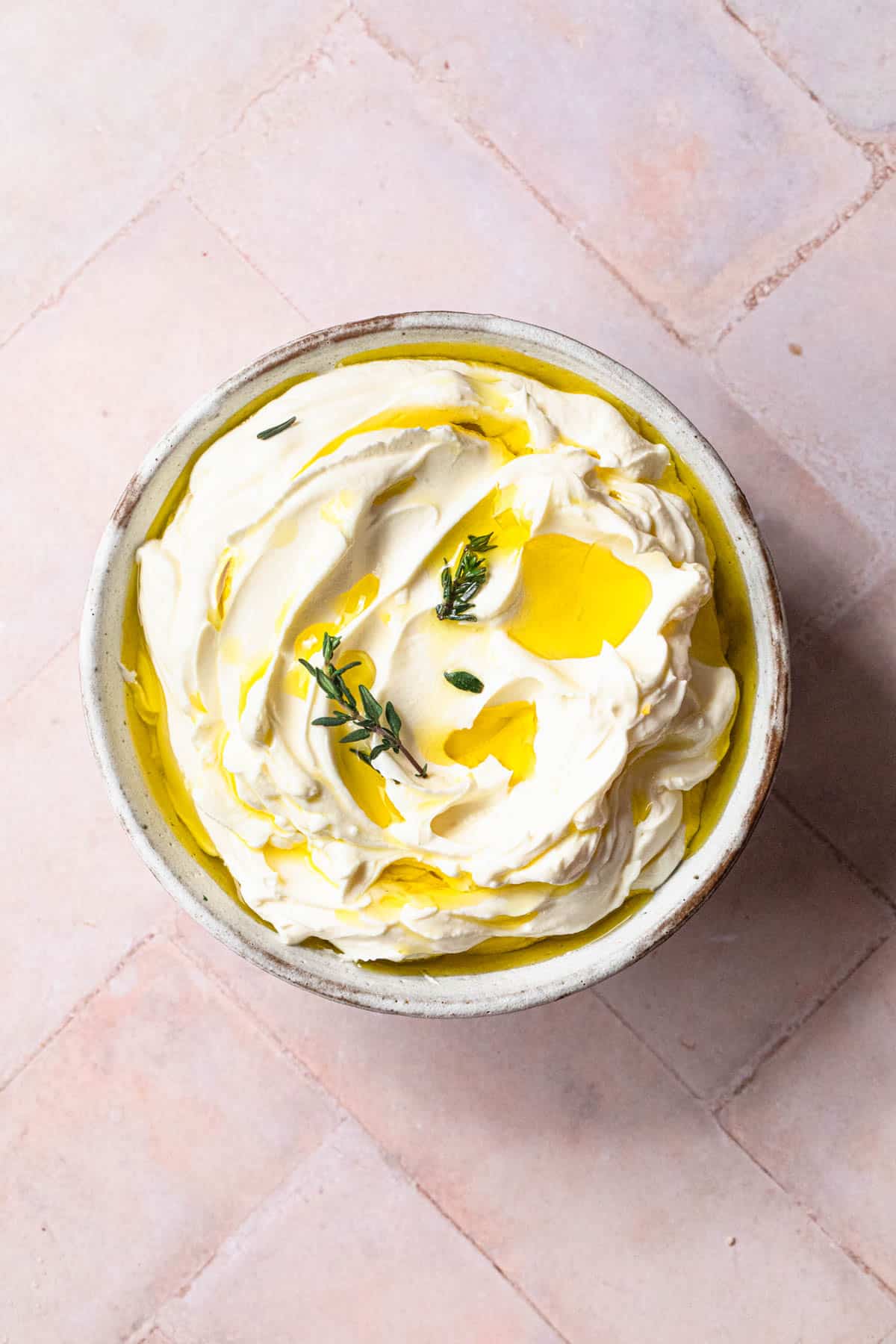 Roasted garlic labneh in a bowl topped with extra virgin olive oil and thyme.