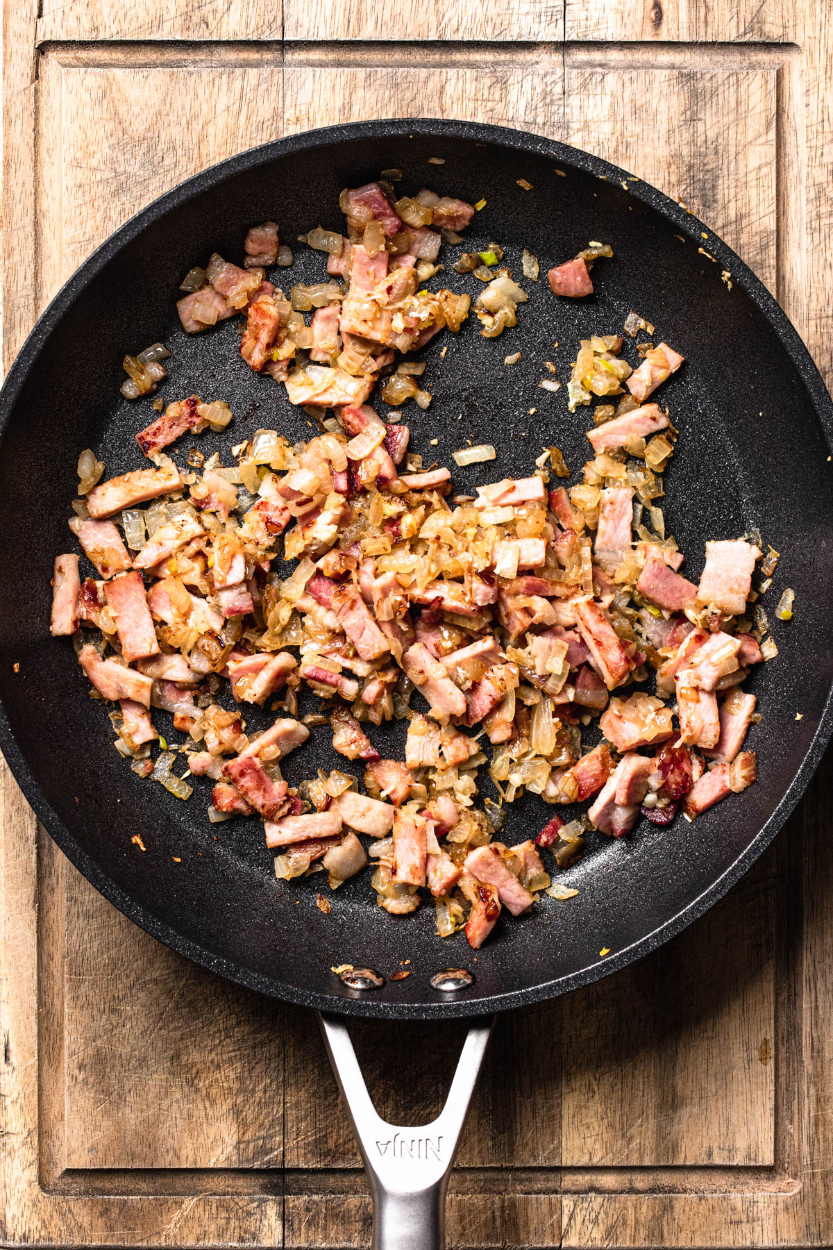 Caramelised diced bacon and onion in a skillet.