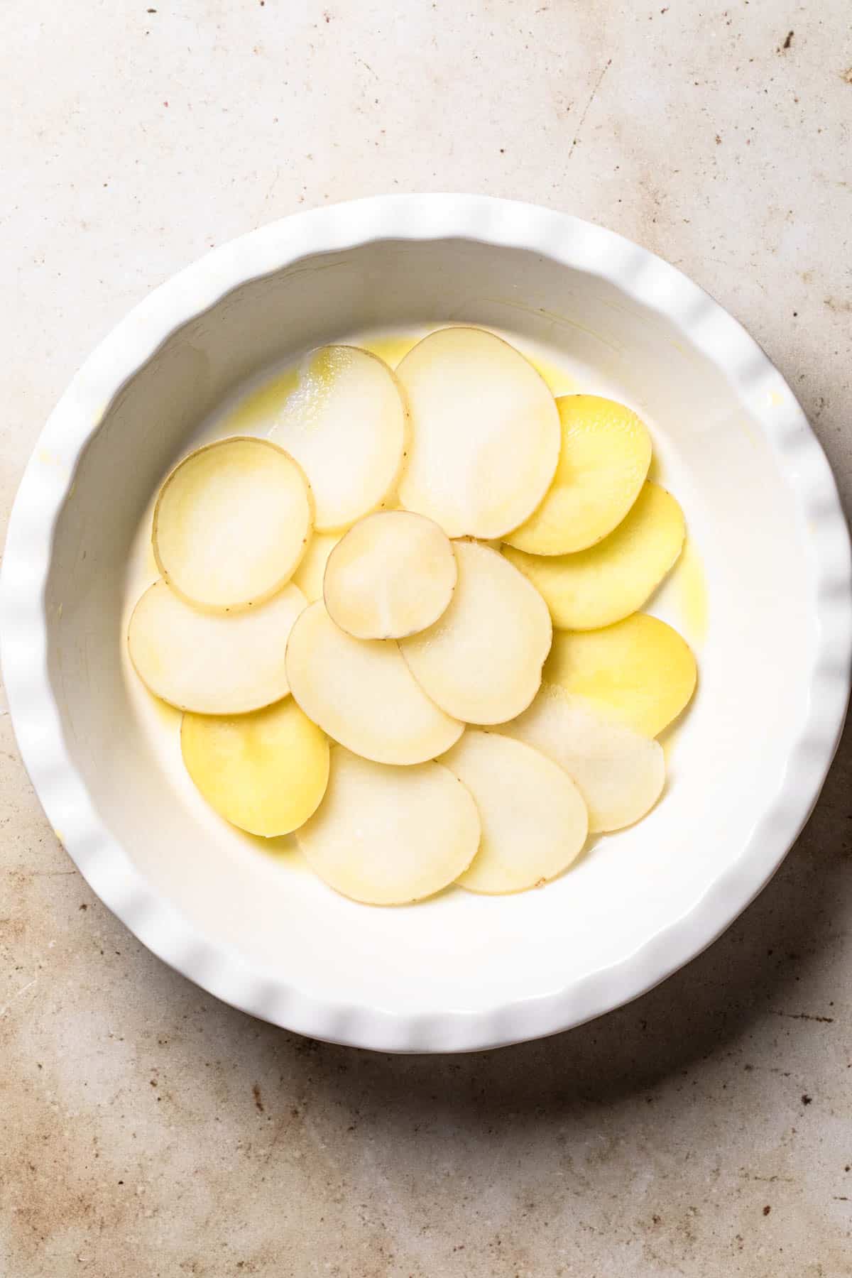 Cooked thin slices of potato in a quiche dish.
