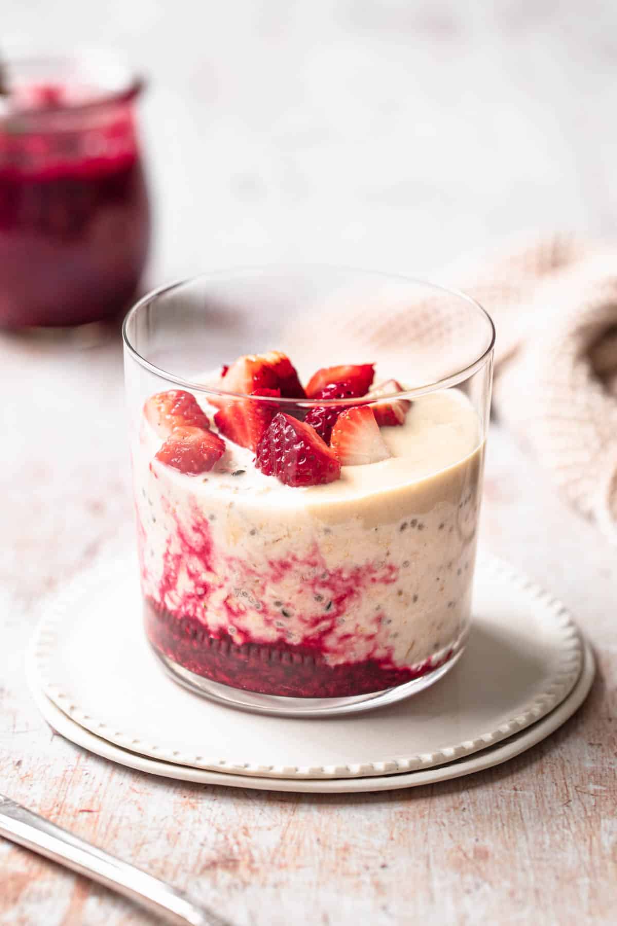 Overnight oats made without milk, in a glass tumbler, layered with raspberry compote and topped with tahini.