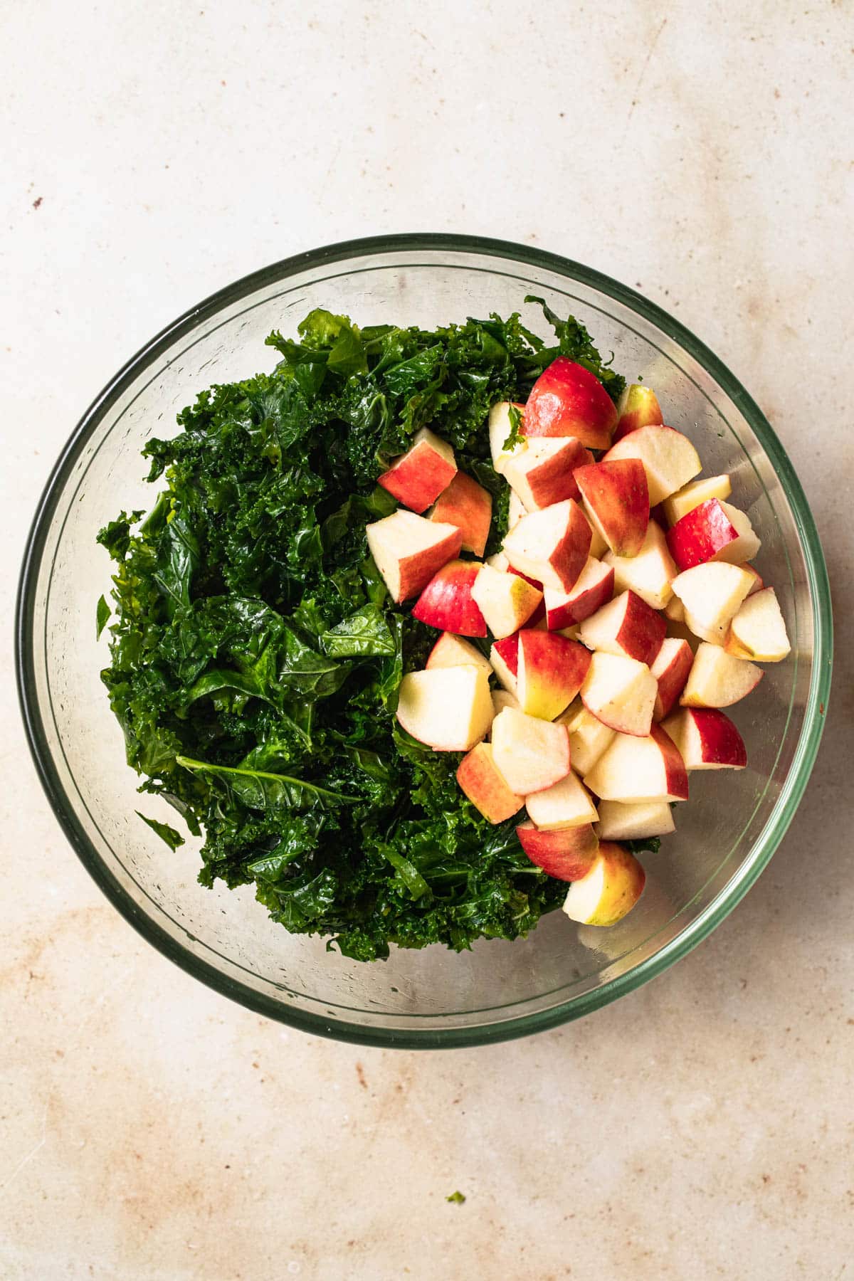 Massaged kale and diced red apples in a bowl.